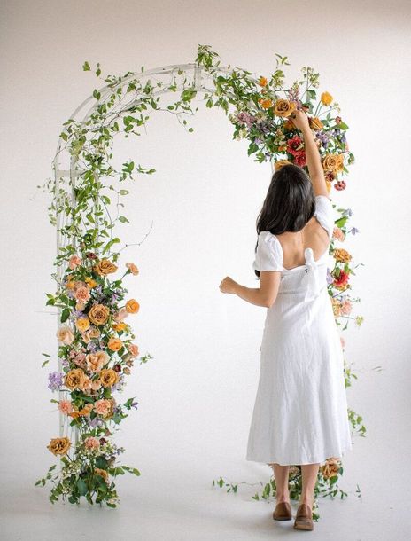 A woman in a white dress is standing in front of a floral arch.