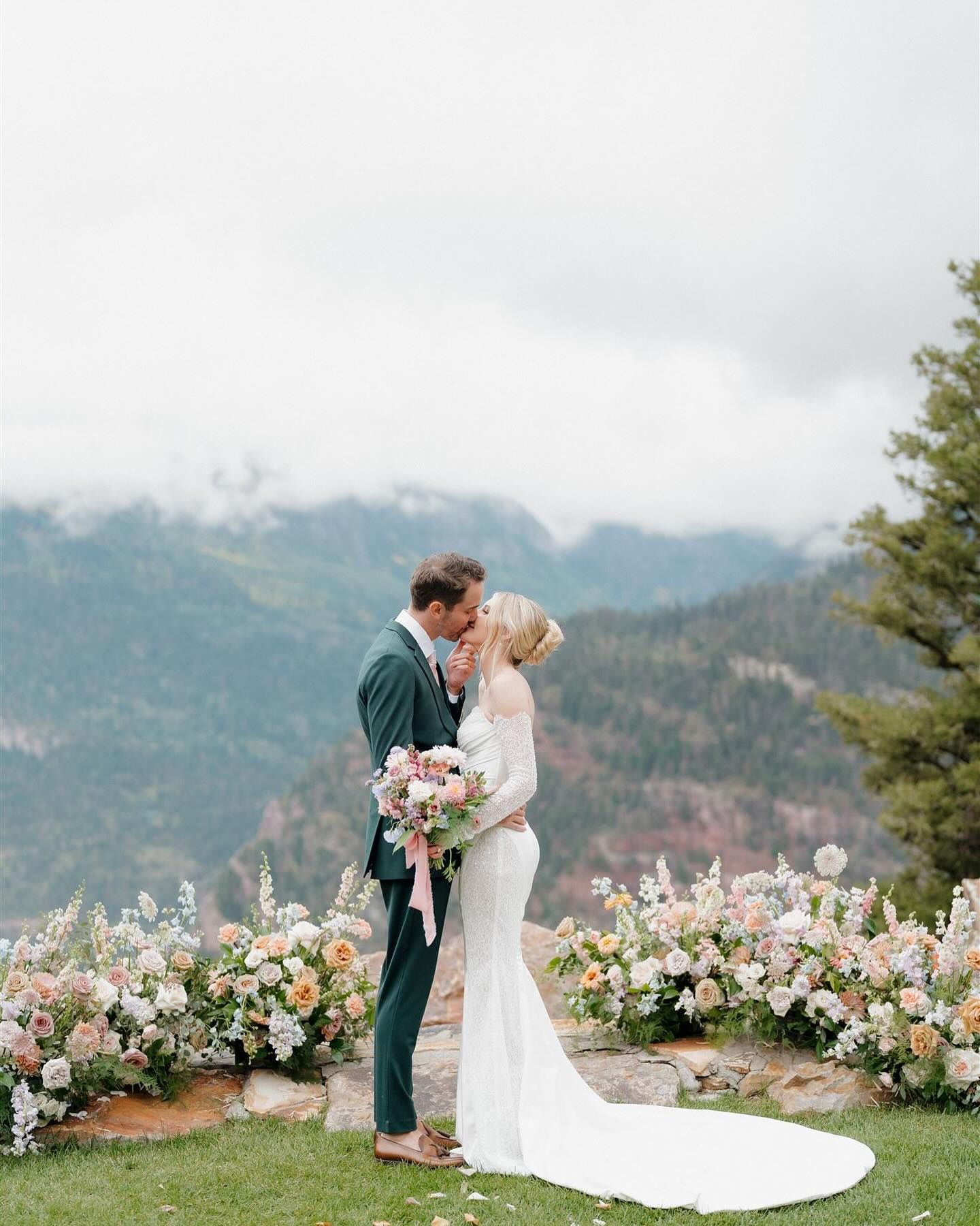 A bride and groom are kissing in front of a mountain range.