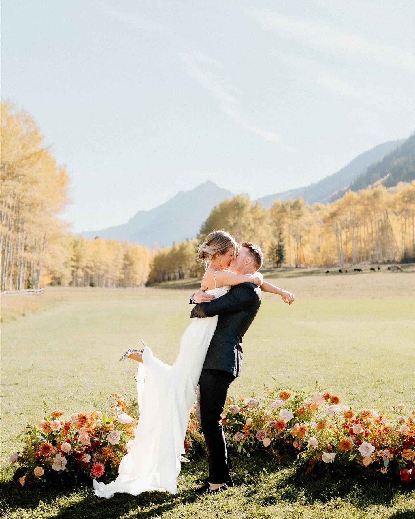 A bride and groom are kissing in a field with mountains in the background.
