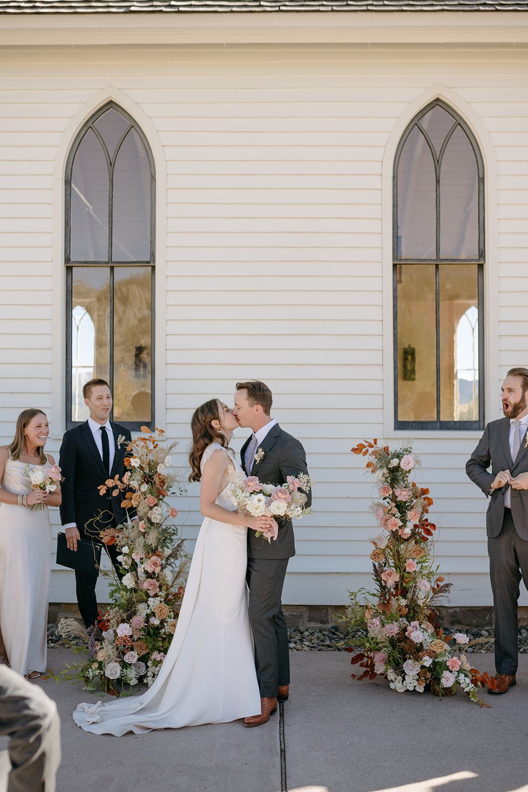 A bride and groom kissing during their wedding ceremony in front of a church.