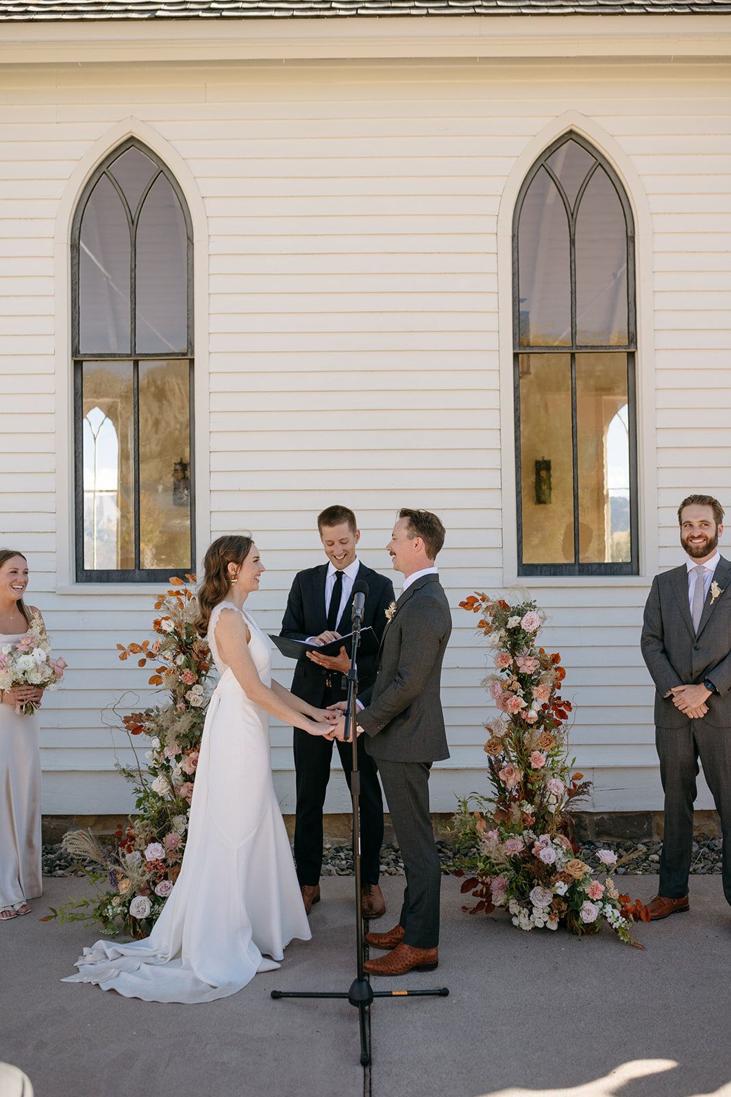 A bride and groom are holding hands during their wedding ceremony in front of a church.