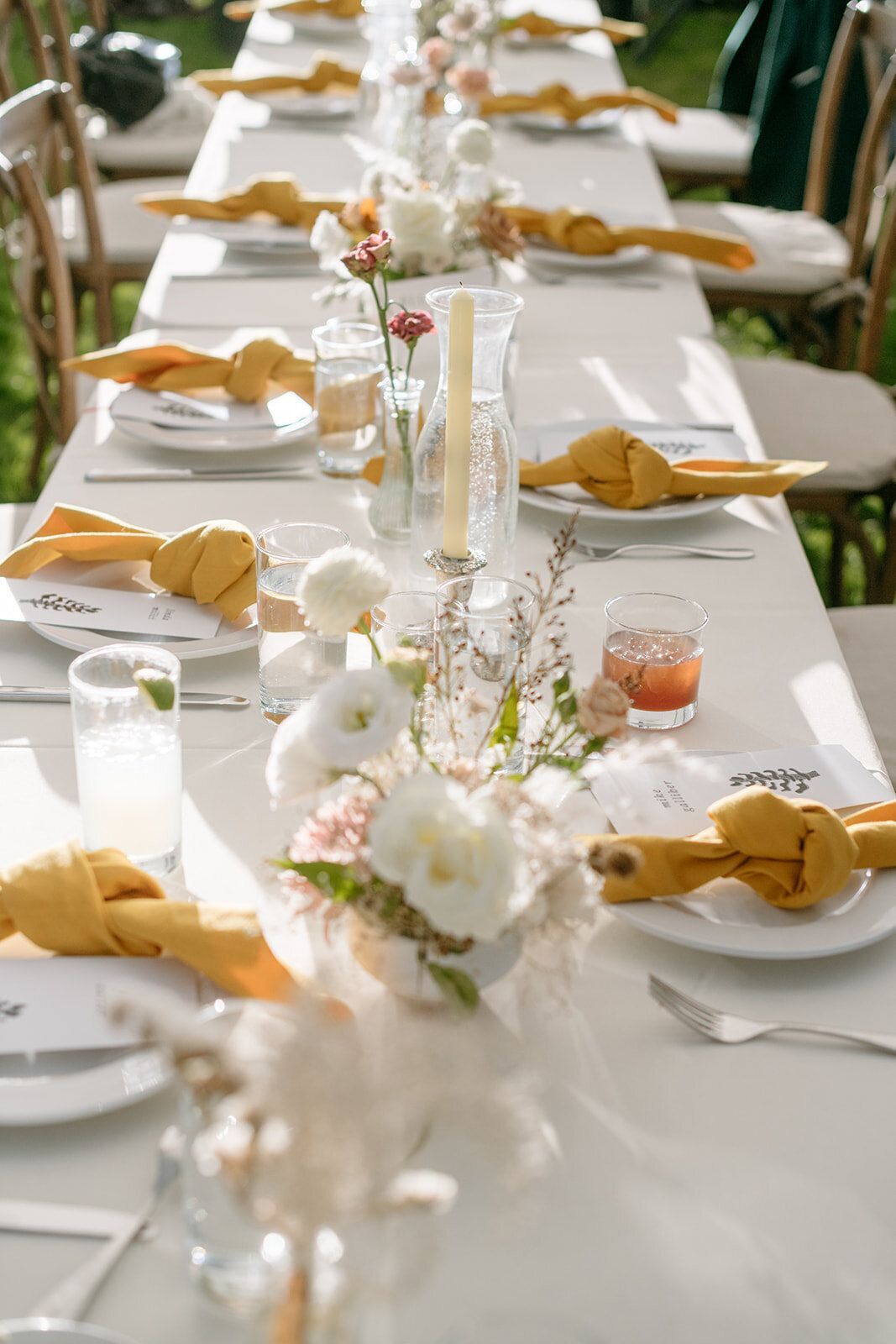 A long table set for a wedding reception with plates , napkins , candles and flowers.