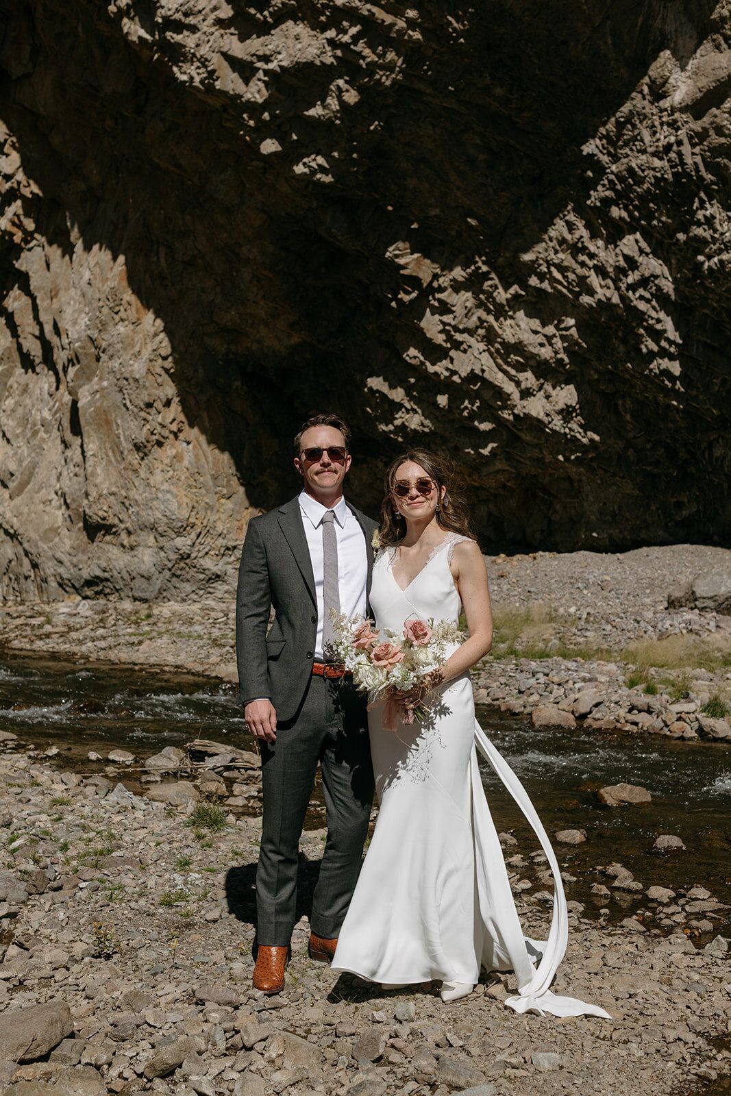 A bride and groom are posing for a picture in front of a river.