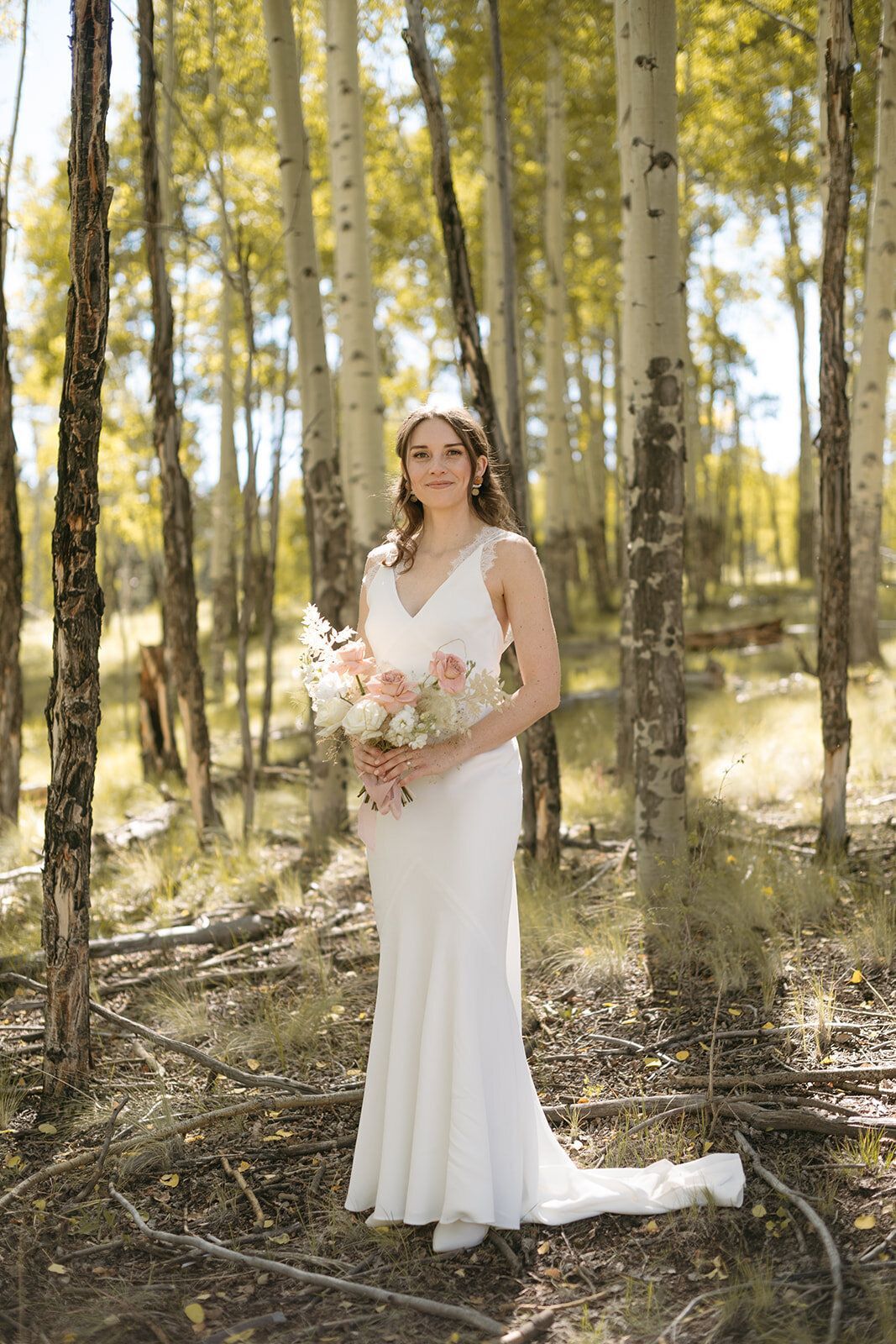 A bride in a white dress is standing in a forest holding a bouquet of flowers.