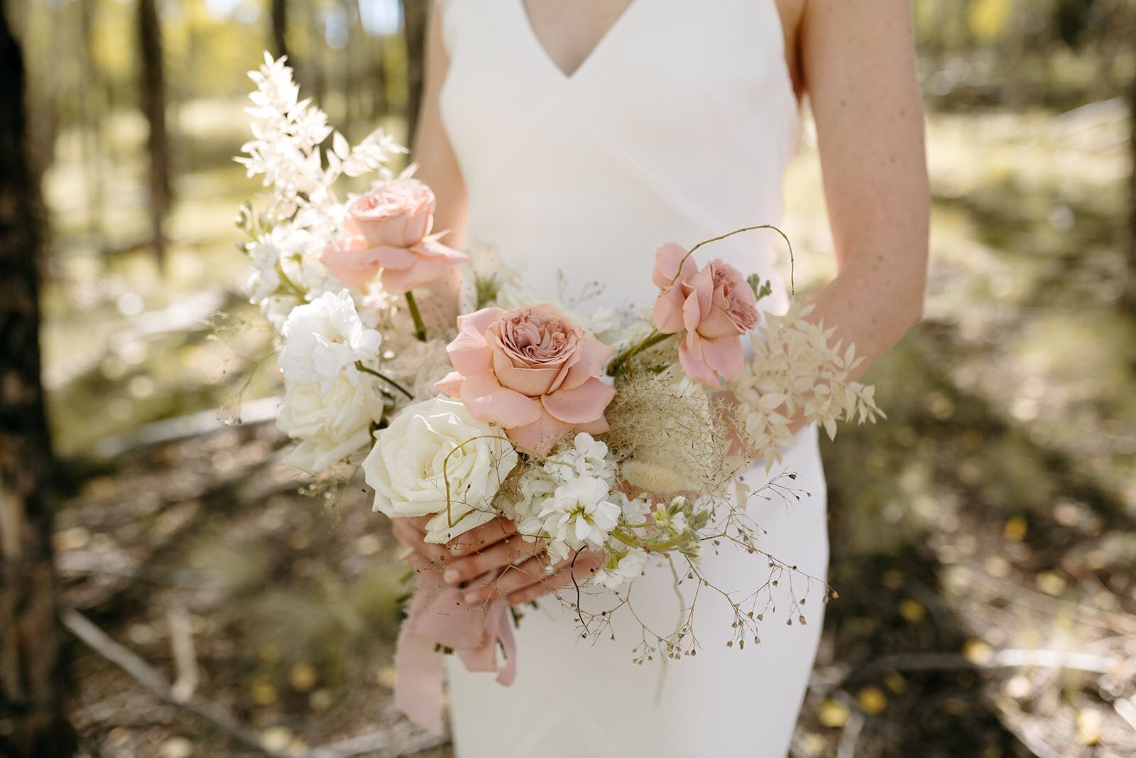 A bride in a white dress is holding a bouquet of pink and white flowers.