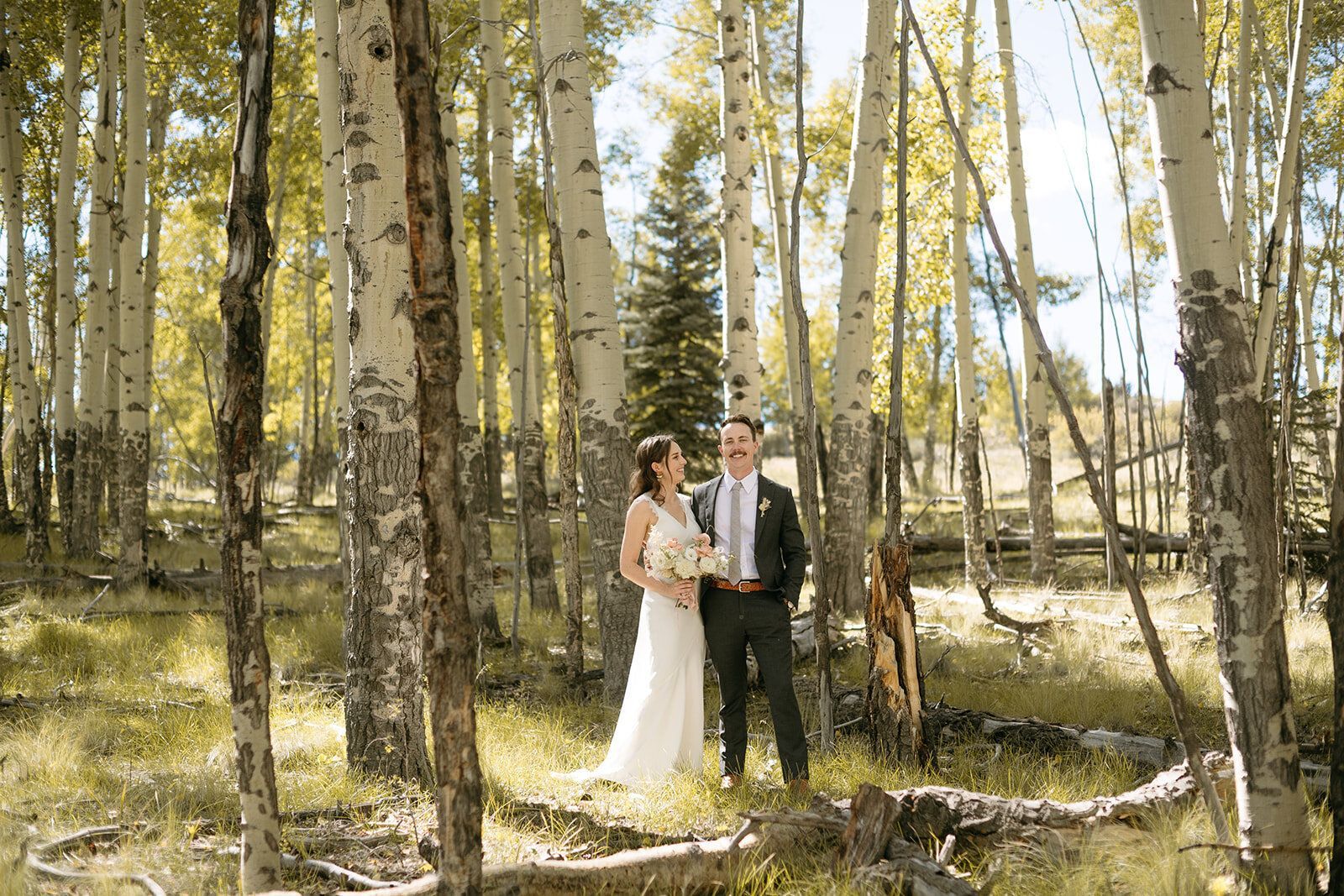 A bride and groom are standing in the middle of a forest.
