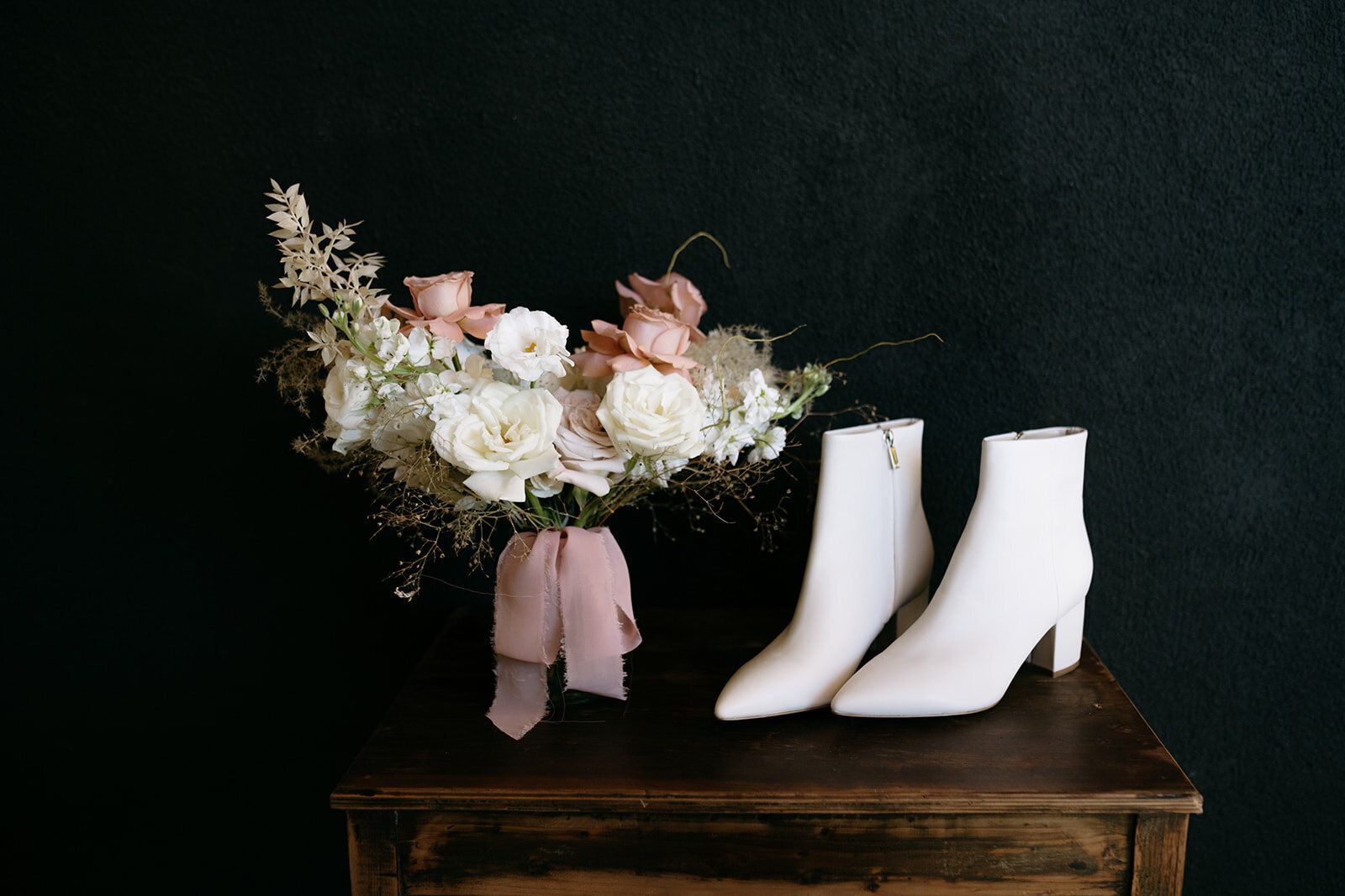 A bouquet of flowers and a pair of white boots are on a wooden table.