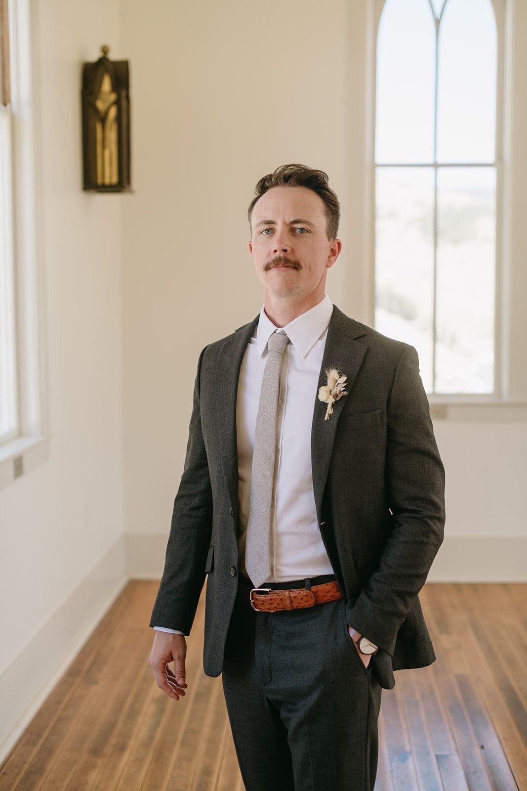 A man in a suit and tie is standing in front of a window.