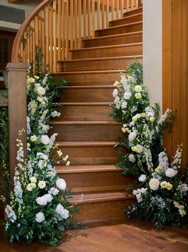 A wooden staircase decorated with white flowers and greenery.