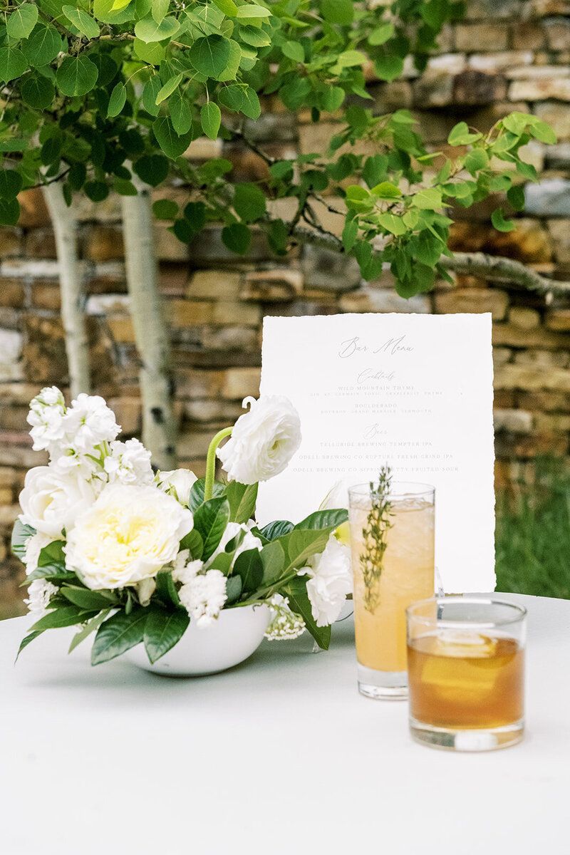 A table with a vase of flowers and two drinks on it.