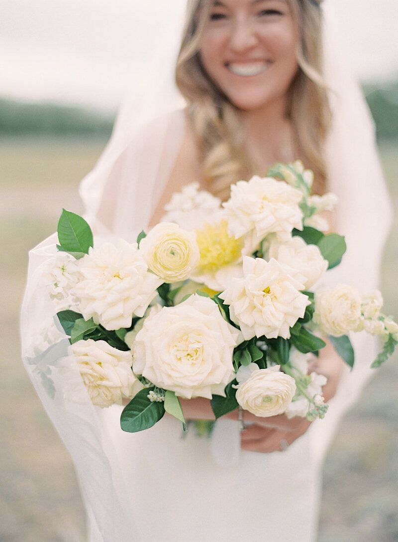 A bride in a white dress is holding a bouquet of white flowers.