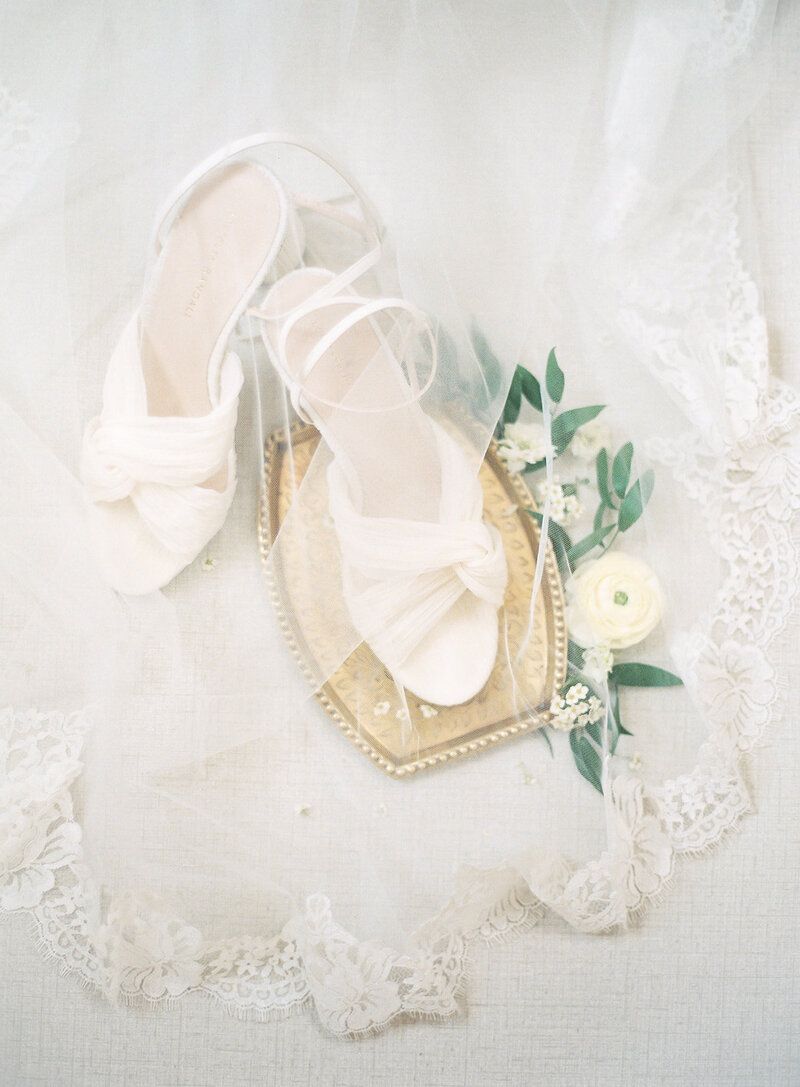 A pair of white wedding shoes sitting on top of a wooden tray.