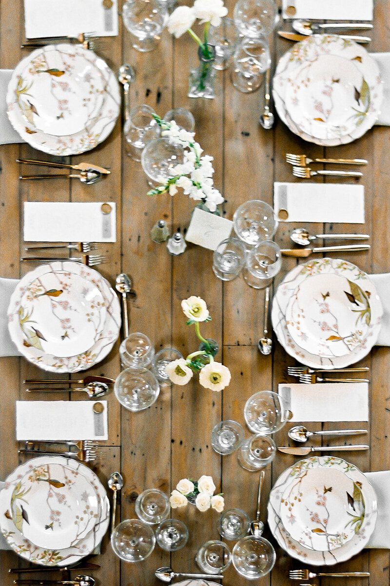A long wooden table with plates , utensils , and flowers on it.