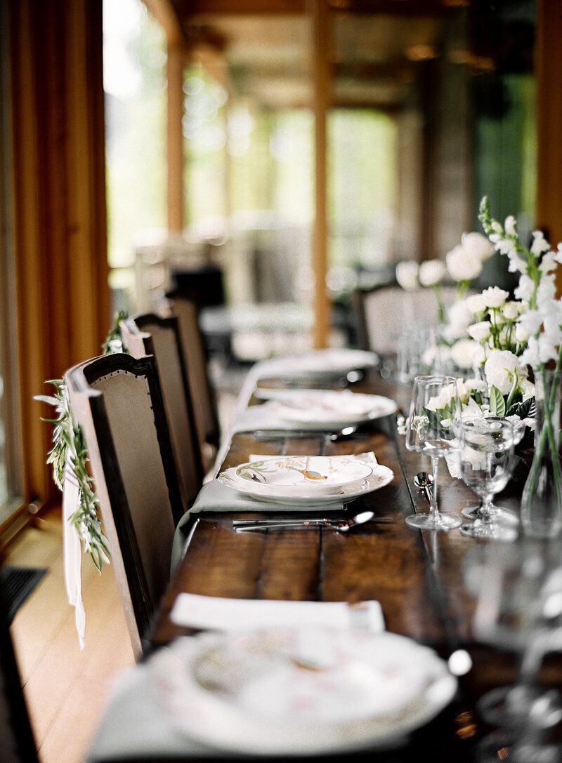 A long table with plates , utensils , and flowers on it.