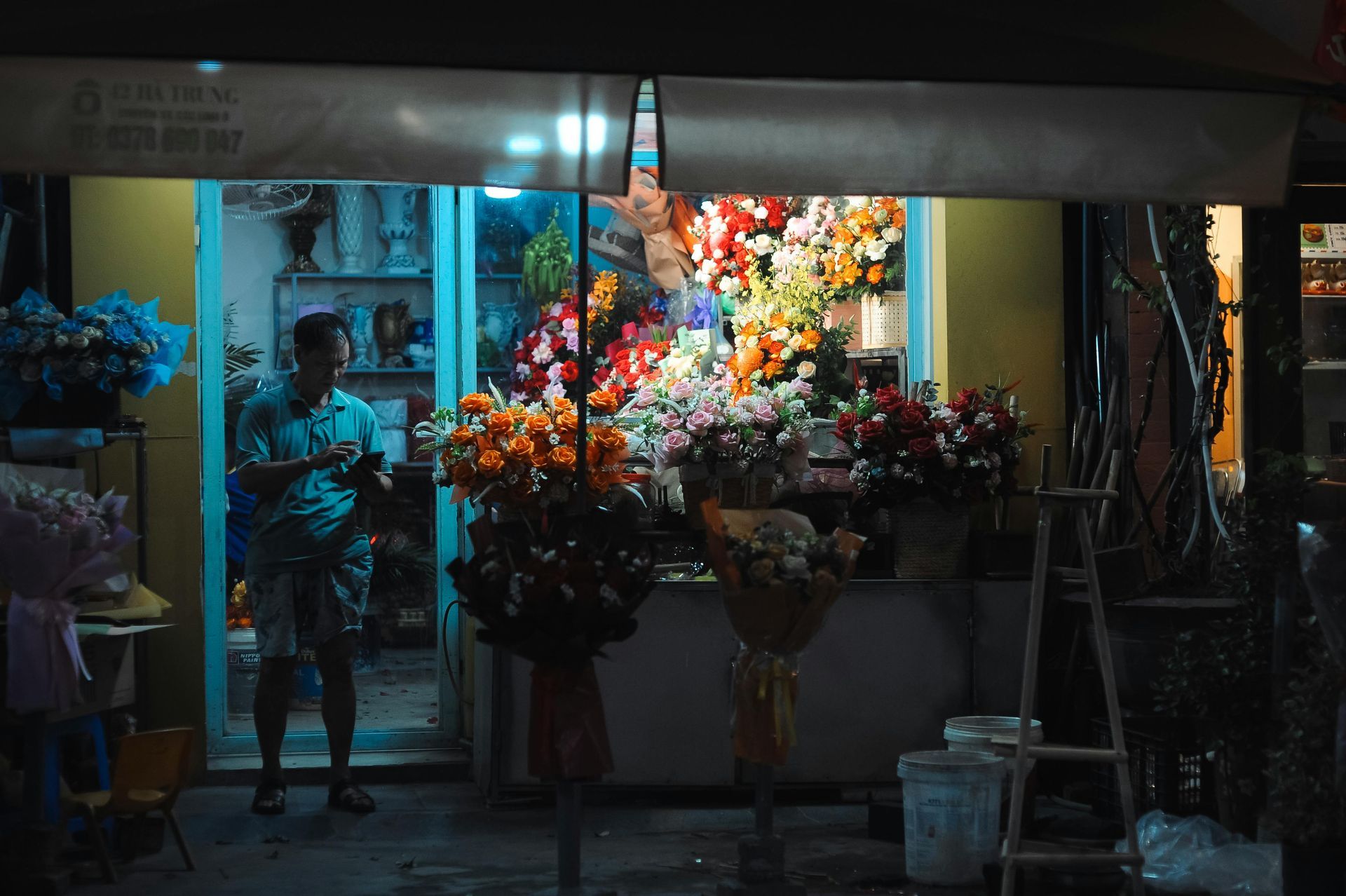 Man inside a flower shop at night with colorful bouquets on display.