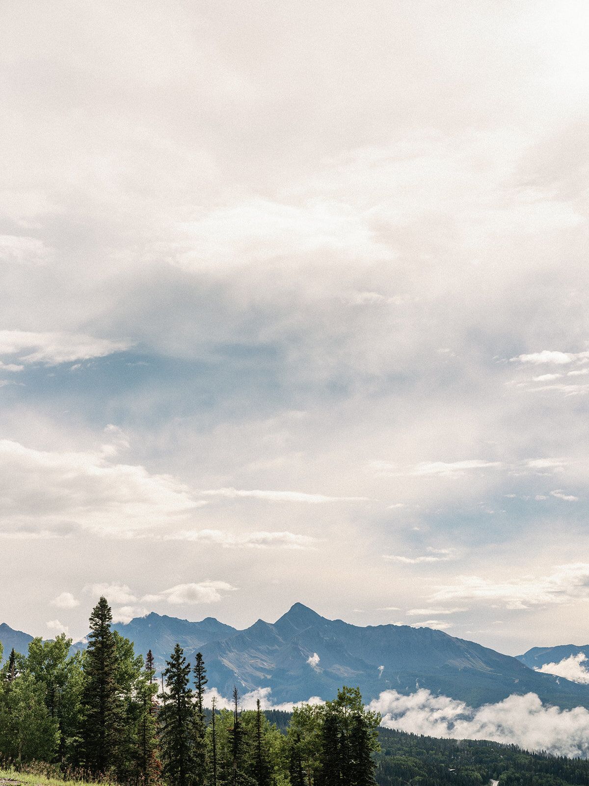 A mountain range with trees in the foreground and clouds in the sky