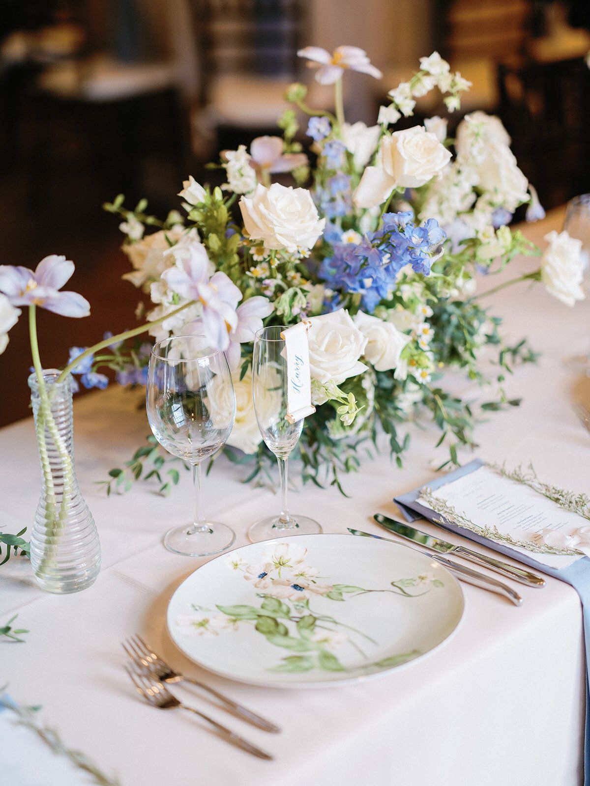 A table with plates , utensils , and a vase of flowers on it.