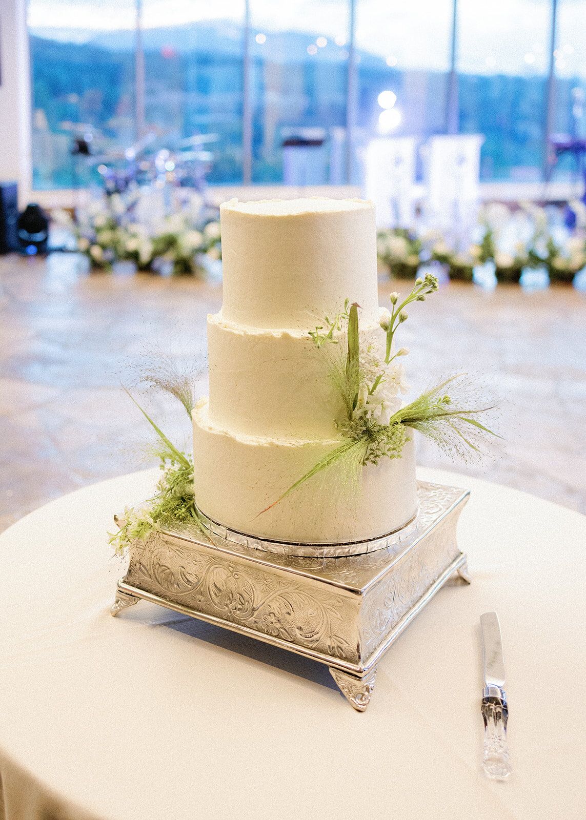 A white wedding cake is sitting on top of a silver cake stand on a table.