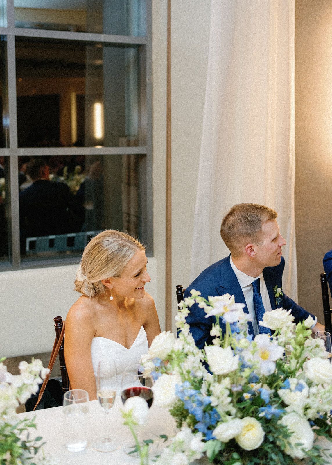 A bride and groom are sitting at a table with flowers.