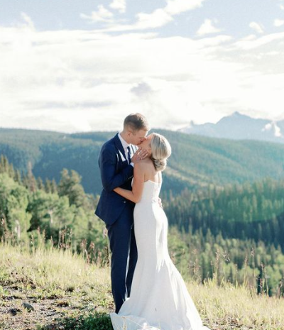 A bride and groom are kissing on top of a hill.