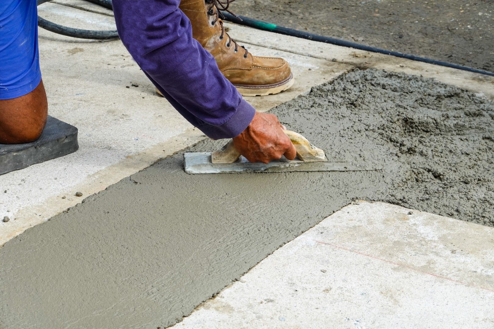 A person is spreading concrete on the ground with a trowel.