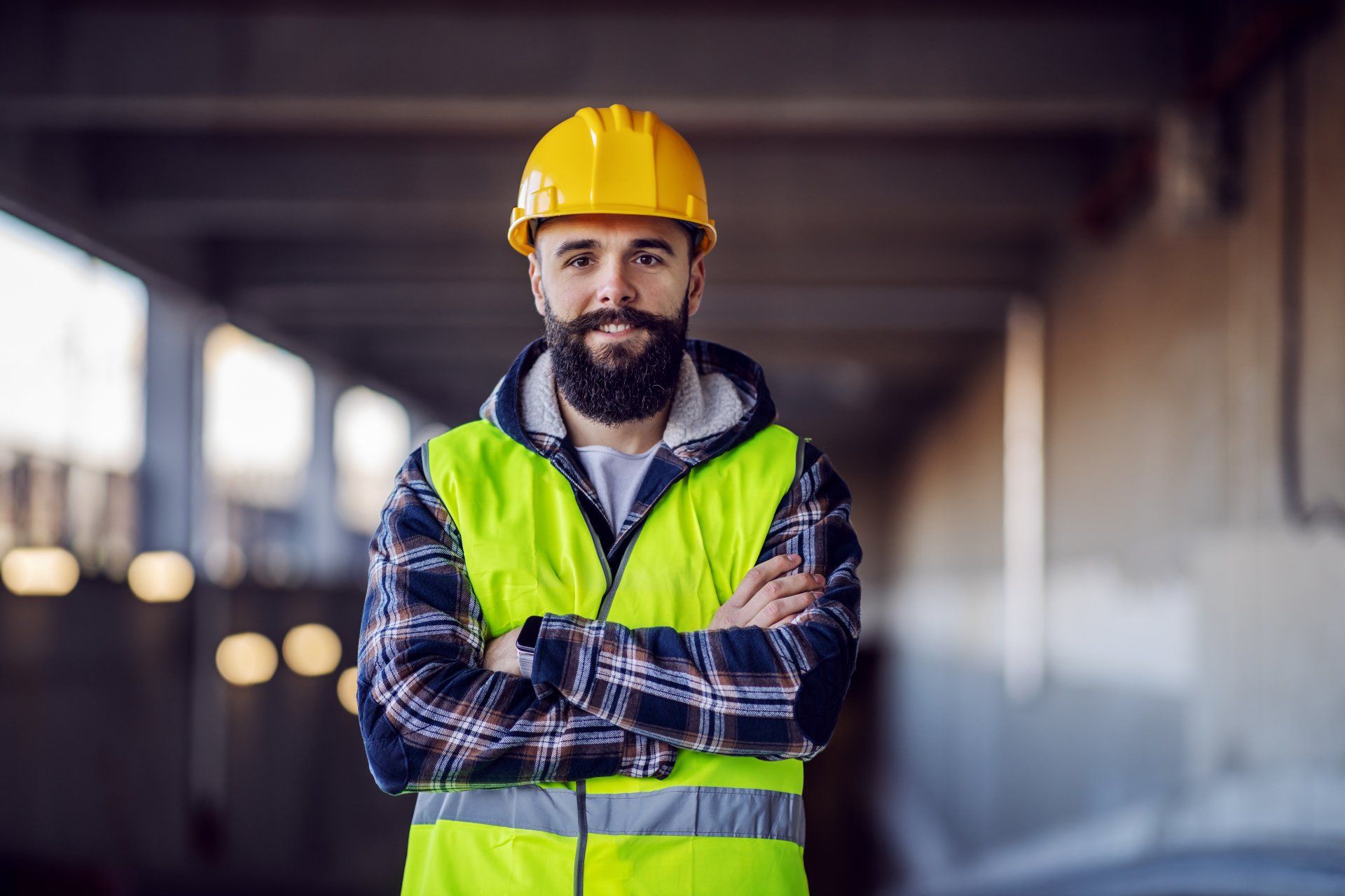Un homme avec une barbe portant un casque et un gilet jaune est debout, les bras croisés.
