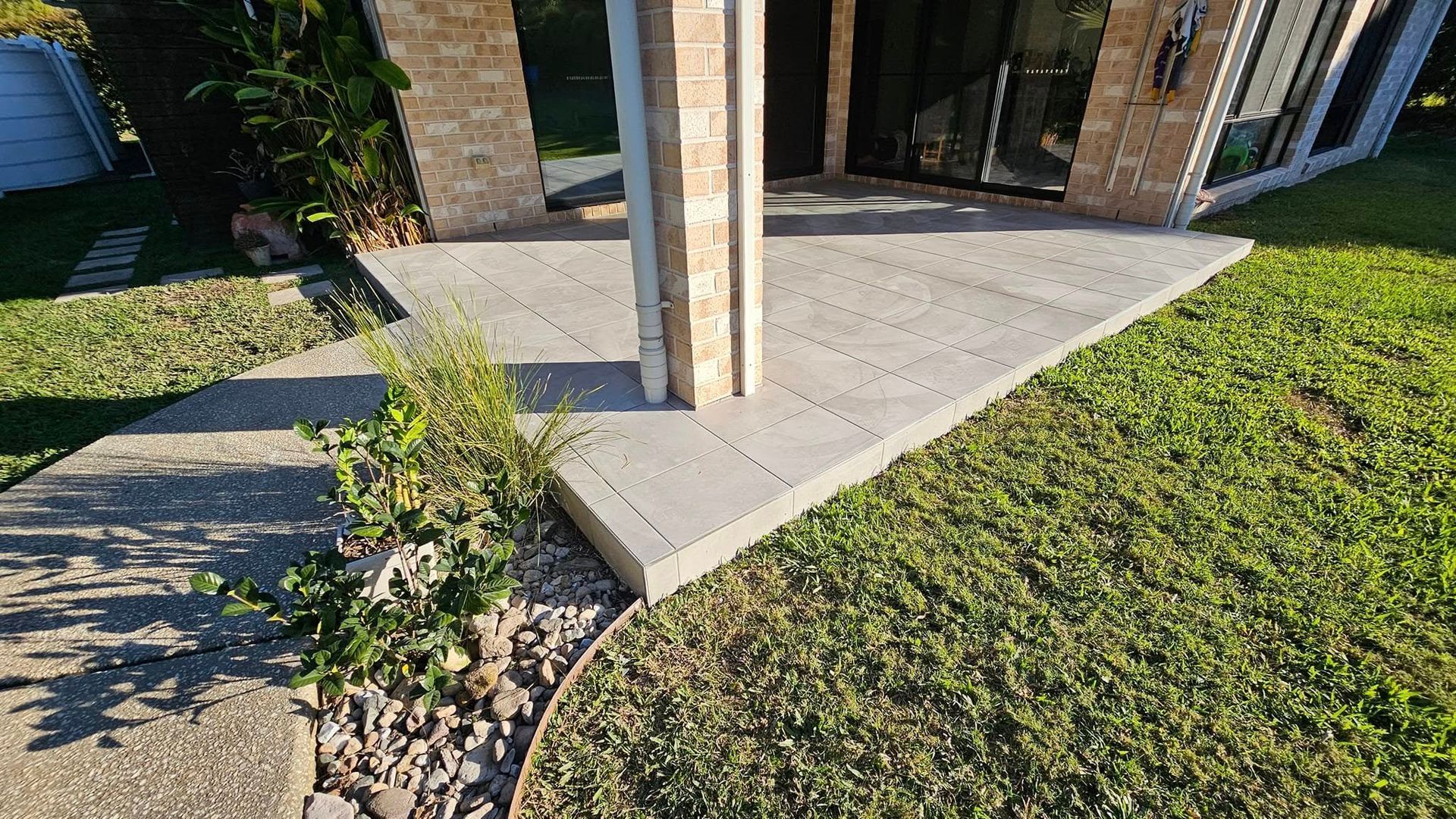 Concrete patio with stone pillars, surrounded by grass, pathway, and small plants — Sunny Tiling Co in Mount Coolum, QLD