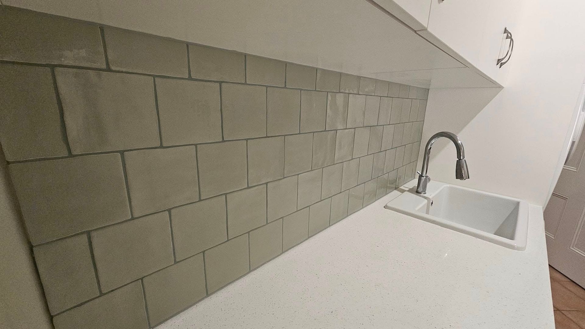 Gray tiled backsplash above a white sink and countertop in a kitchen.