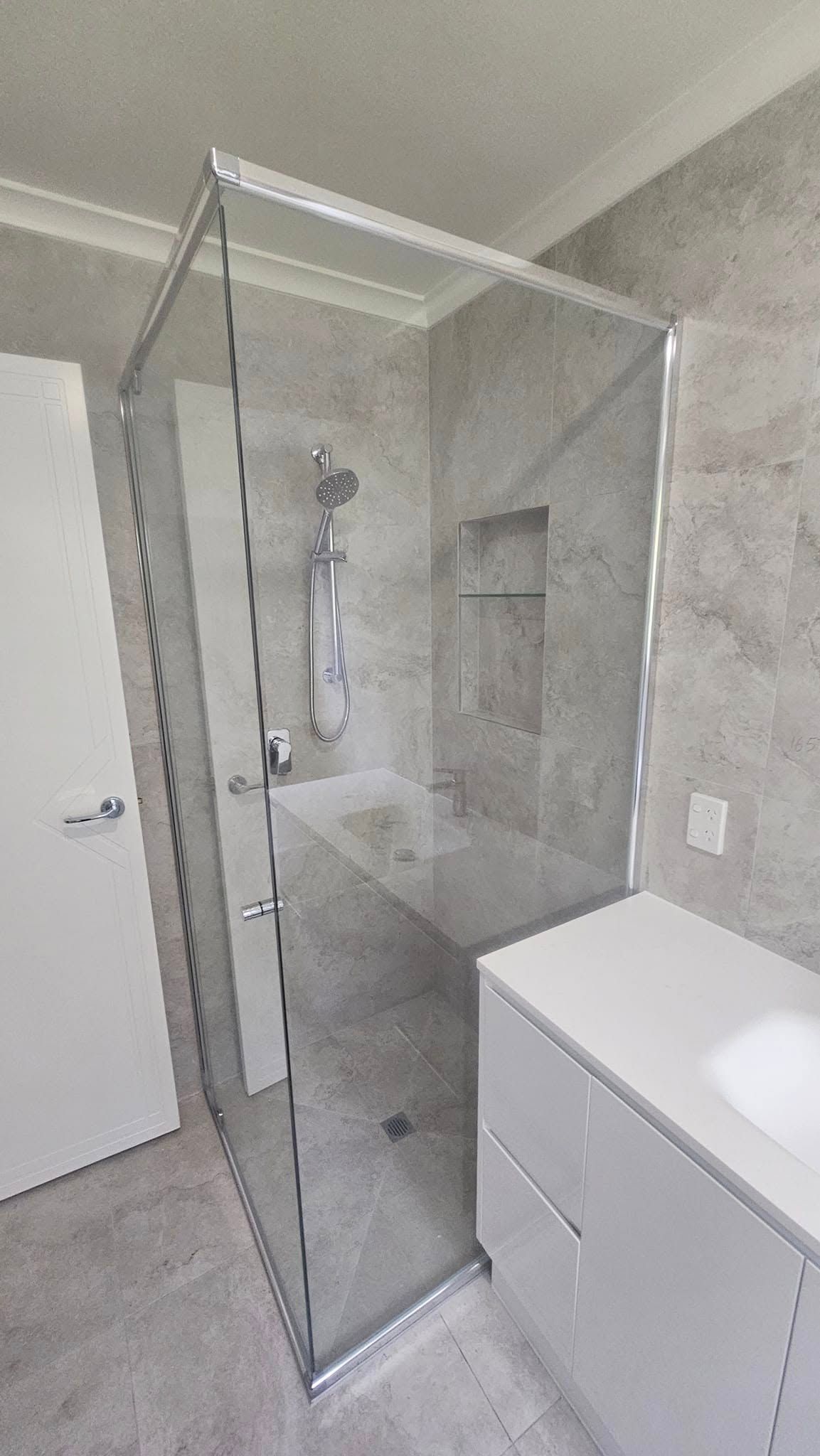 A modern bathroom with a glass shower enclosure and white vanity. Gray stone-like walls.