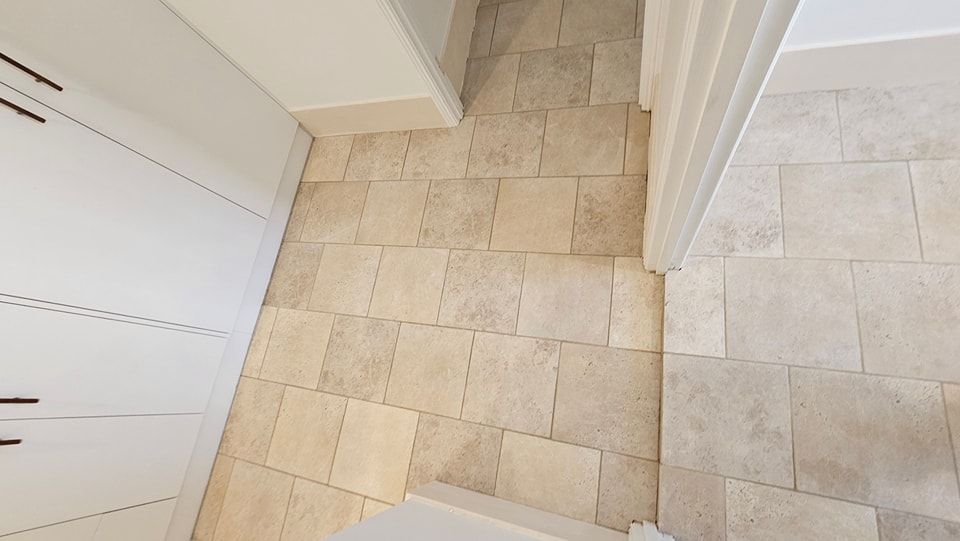 Beige tiled floor in a hallway, next to a white cabinet and doorframe.