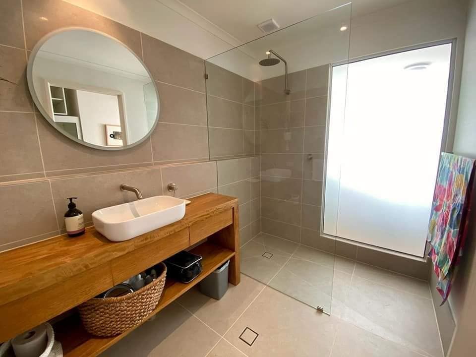 Bathroom With Wooden Vanity, White Sink, Round Mirror, Glass Shower — Sunny Tiling Co in Mount Coolum, QLD
