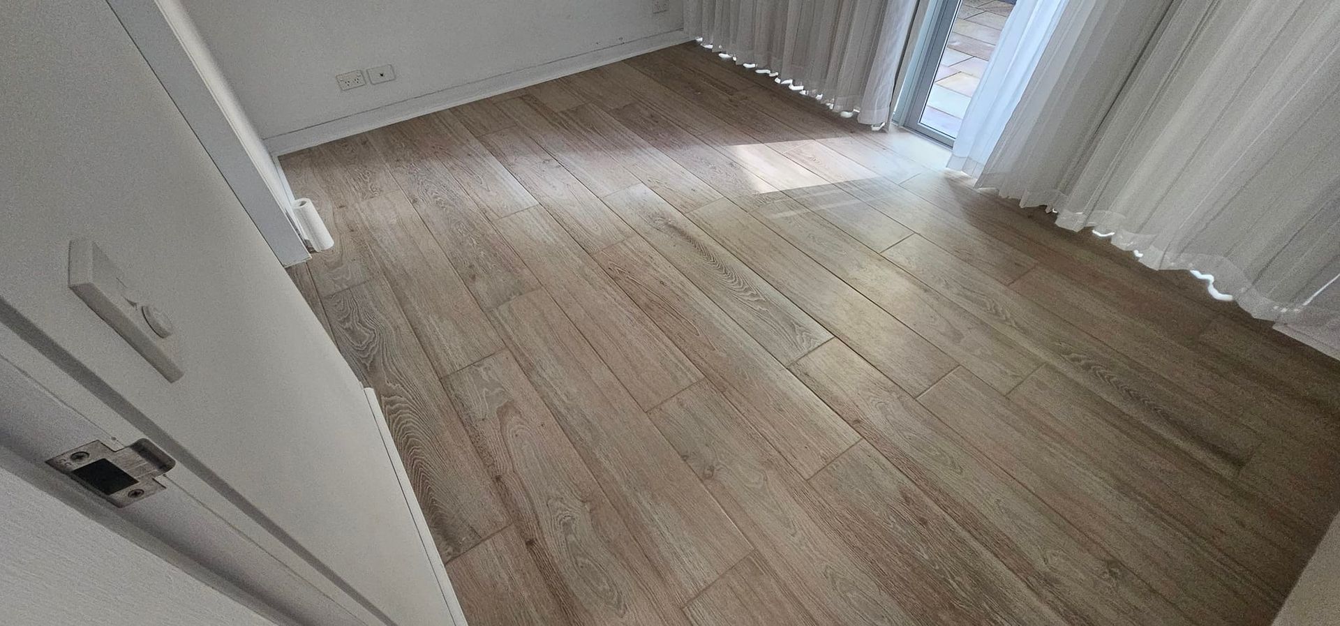 Wooden floor in a bright room, with light coming through a sheer curtain — Sunny Tiling Co in Mount Coolum, QLD