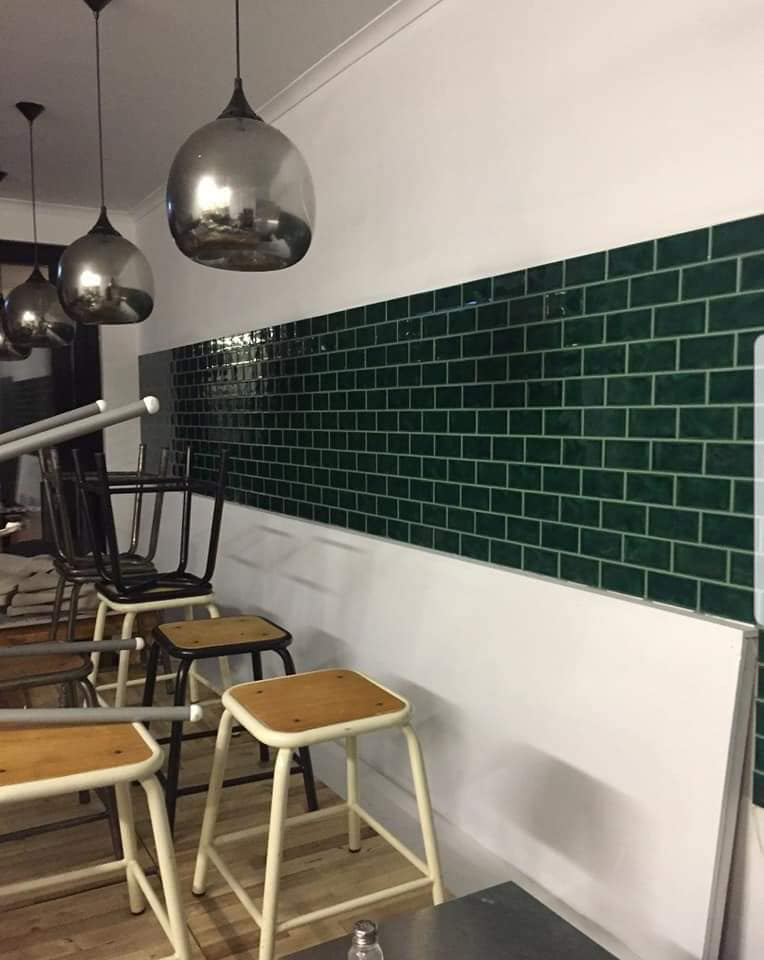 Restaurant interior with emerald green tiled wall, silver pendant lights, stools — Sunny Tiling Co in Mount Coolum, QLD