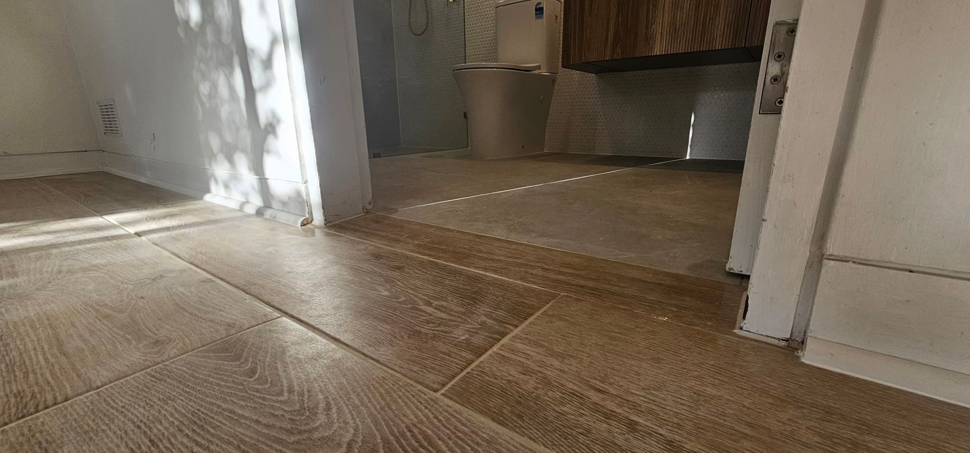 Wood flooring with sunlight casting shadows in a doorway — Sunny Tiling Co in Mount Coolum, QLD