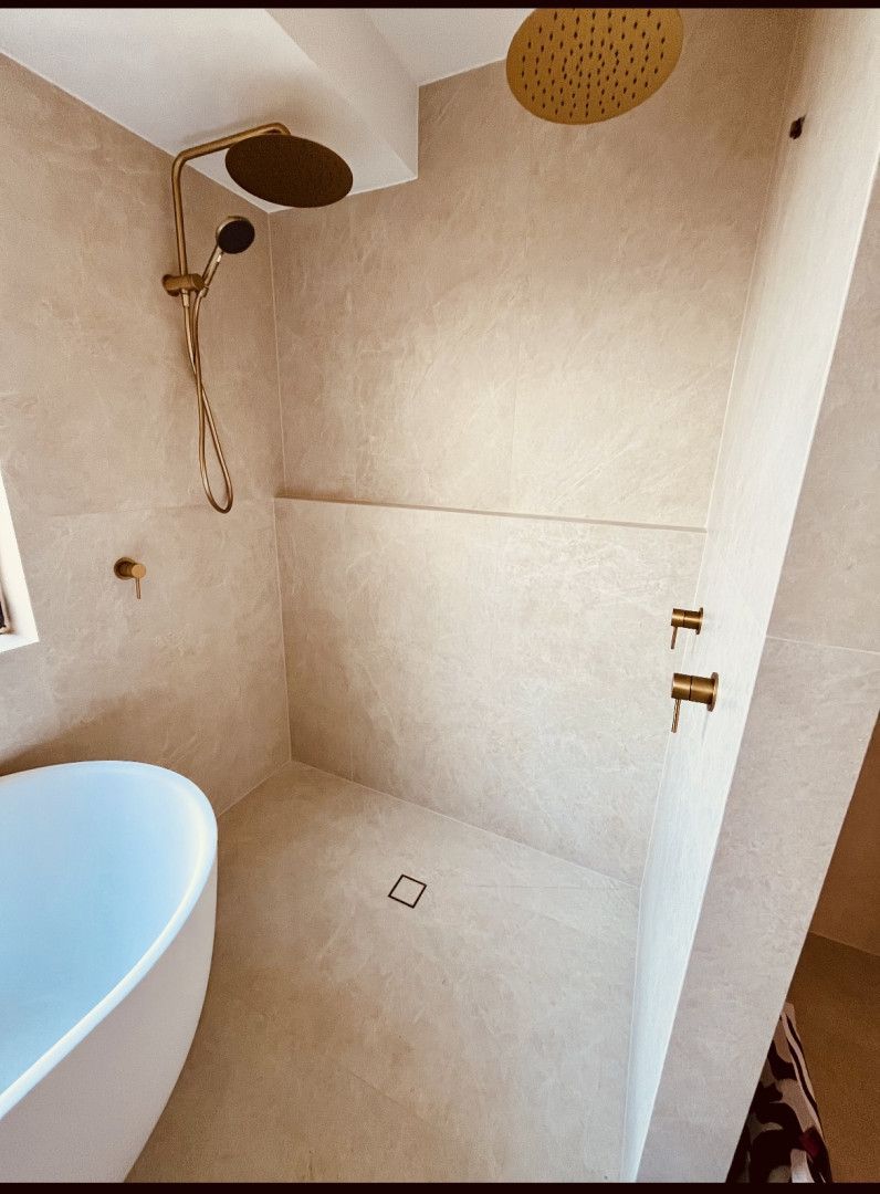 Bathroom with beige walls, gold fixtures, and a white bathtub.