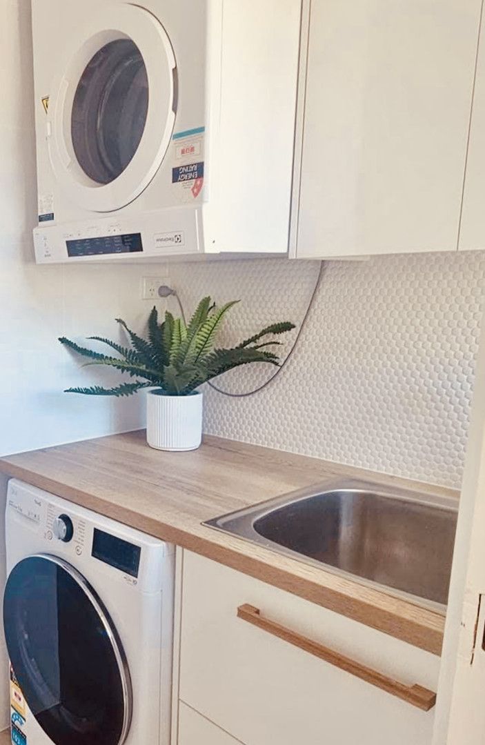 Laundry room with stacked washer/dryer, countertop, sink, and plant.