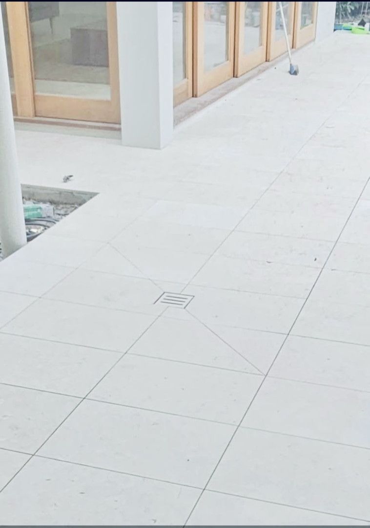 White tiled outdoor walkway with a drain, alongside a building with wooden doors.
