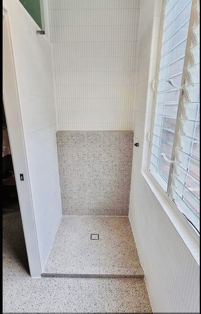 Accessible shower stall with terrazzo-style flooring and white tiled walls; a window with blinds is on the right.