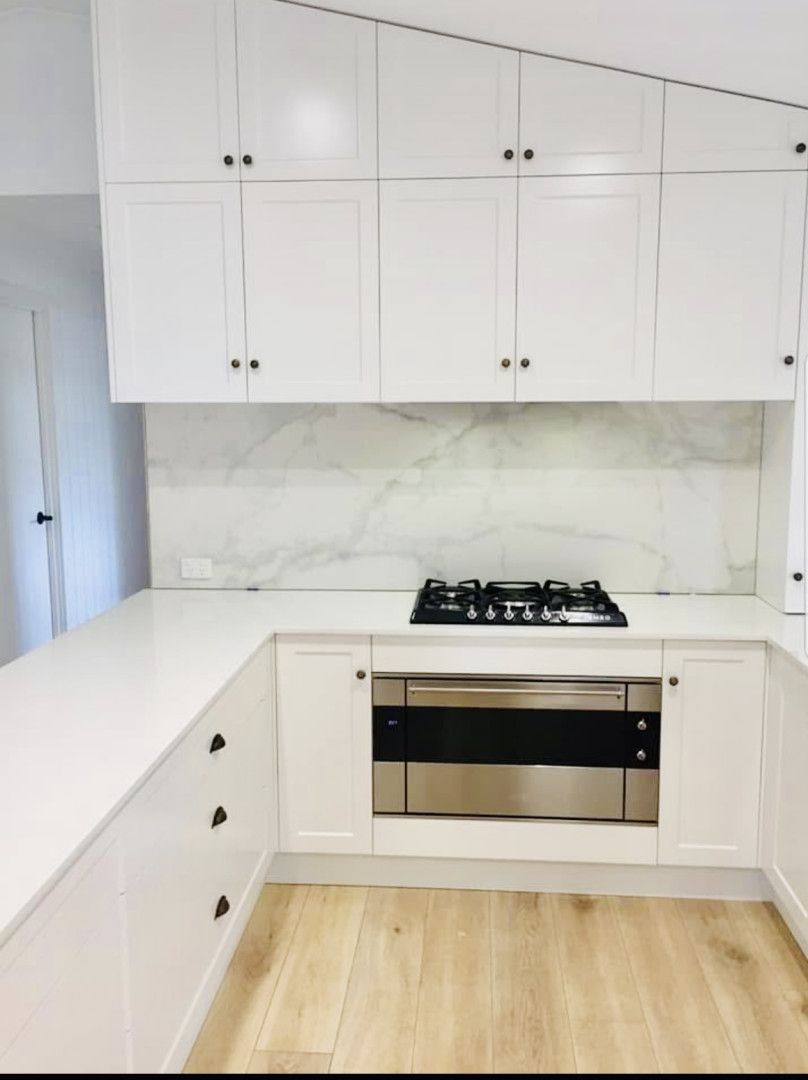White modern kitchen with upper cabinets, marble backsplash, and gas cooktop.