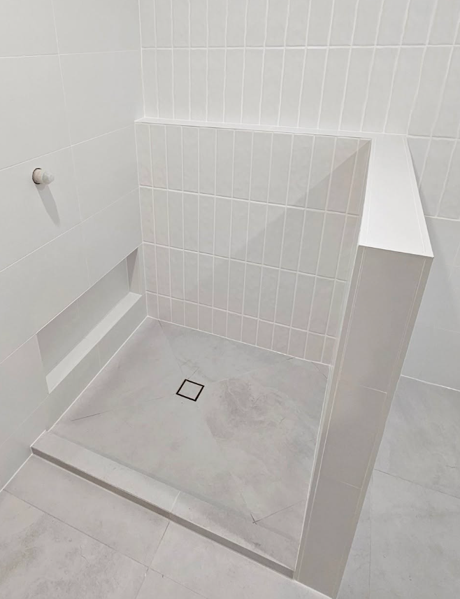 Gray tiled shower with a low entry, drain, and built-in shelf; white walls.