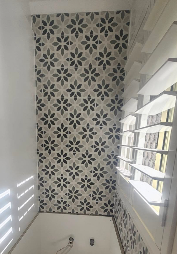 Patterned floral tile wall next to a window with closed white shutters.