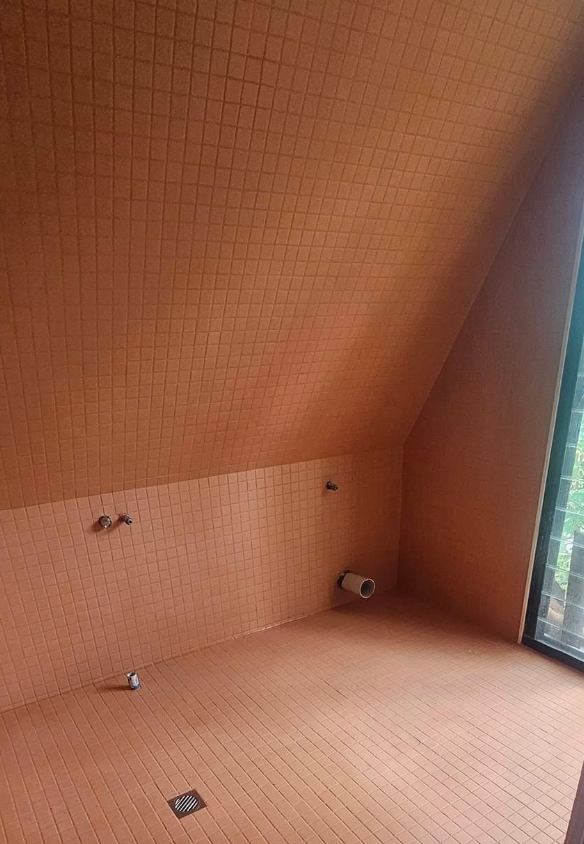 Interior of a tiled bathroom with an angled ceiling, featuring an orange color scheme and a window.