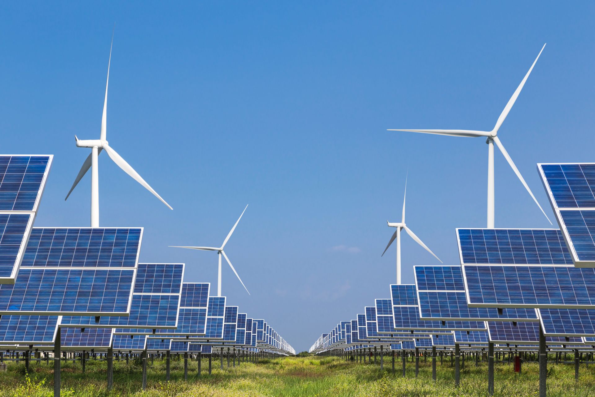 Solar panels and wind turbines in a field, generating renewable energy under a clear blue sky.