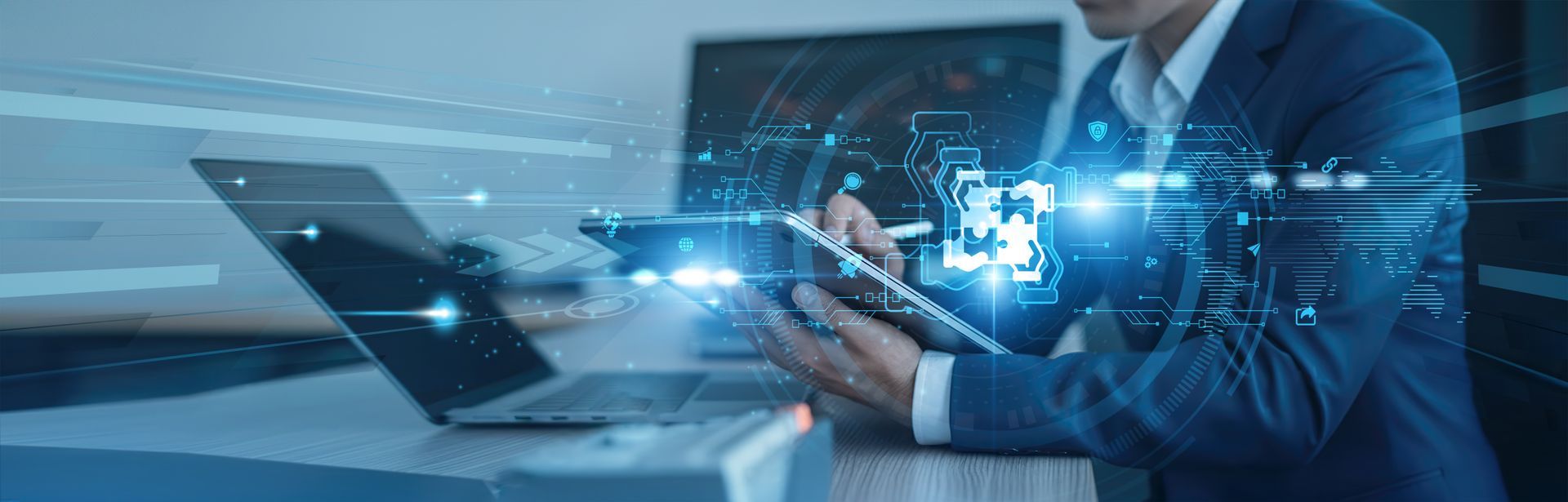 A person in a suit works on a tablet, with a laptop open next to it, blue digital effects.