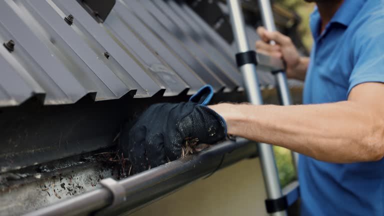 A man is cleaning a gutter on the roof of a house.
