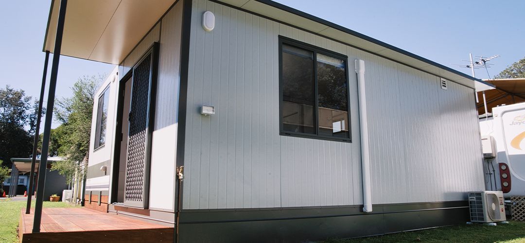 A cabin with a wooden deck and a campervan parked beside it on a grassy area.