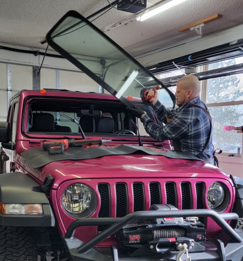 A man is installing a windshield on a pink jeep