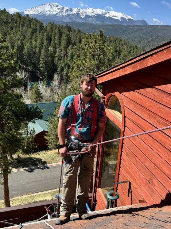 A man is standing on the roof of a building with mountains in the background.