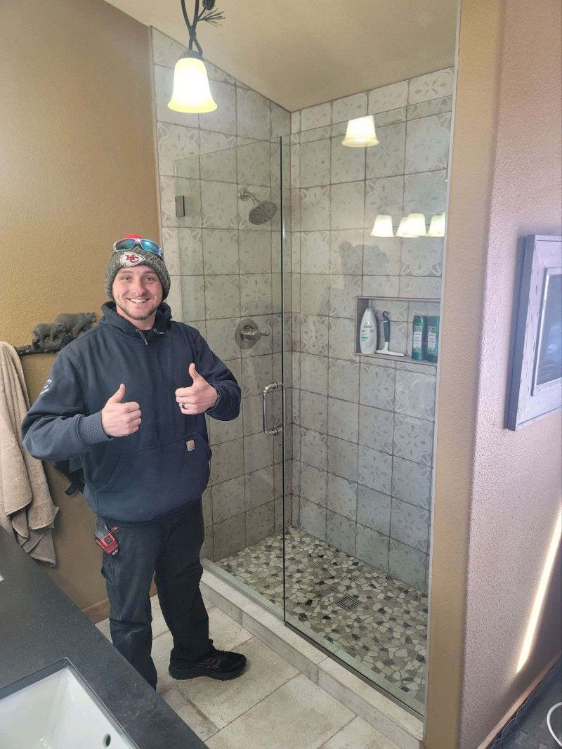 A man is standing in a bathroom next to a shower giving a thumbs up.