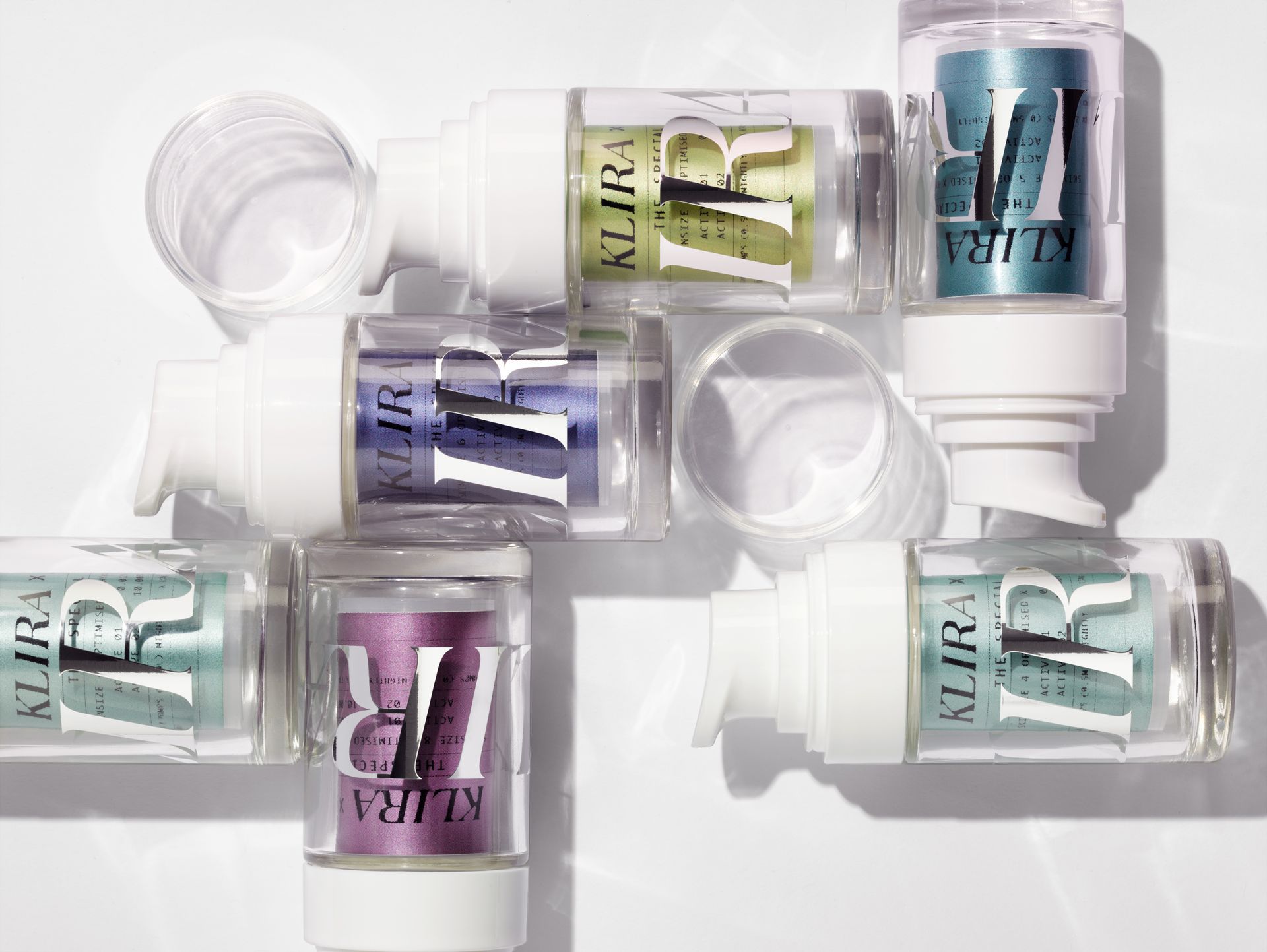 Clear plastic cosmetic bottles with white pumps and colorful product inside, arranged on a white surface.